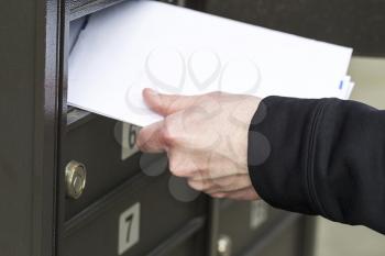 Horizontal photo of male hand pulling out letters from postal mailbox