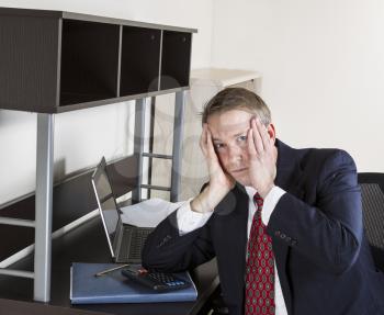 Mature man stressed out at work with computer, calculator, pen and papers on desk