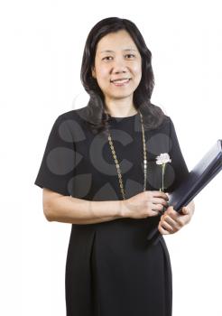 A portrait Vertical photo of a mature Asian woman wearing a dark dress while holding a single flower and folder isolated on white background