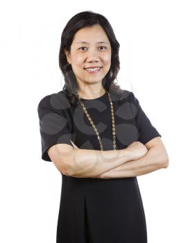 A vertical portrait photo of a mature Asian woman wearing a dark dress with arms crossed while smiling on white background