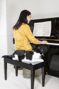 Vertical photo of mature woman playing piano with her family pet cat sitting right next to her side whiles she is performing