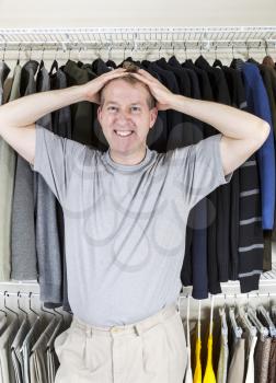 Vertical portrait of mature Caucasian man in walk-in closet showing frustration with hands behind head while pulling his hair