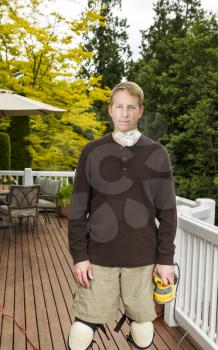 vertical photo of mature man preparing to sand outdoor wooden deck with patio furniture and trees in background