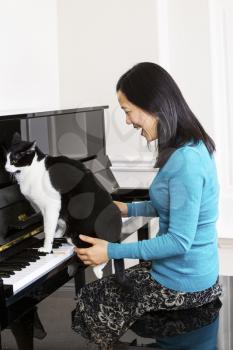 Vertical photo of mature woman laughing at family cat sitting on piano keyboard
