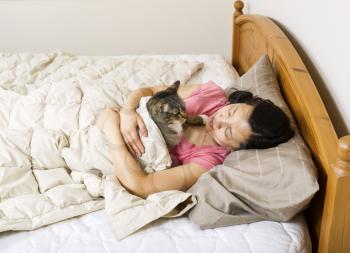 Horizontal photo of mature woman, lying head down in pillow, while looking into the face of her family cat