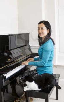 Vertical photo of mature woman with her family cat at her side while sitting at the piano