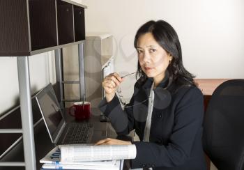 Mature Asian woman in the process of doing income taxes with tax form booklet, calculator, coffee cup and computer on desk