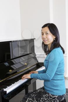 Vertical photo of mature woman playing piano with white walls in background