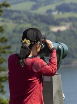 Vertical photo of mature woman looking through telescope at Columbia River Gorge located in the Northwest section of the United States