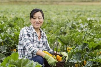 Mature women sitting in vegetable field with basket full of zucchini and cucumbers