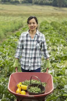 Mature women holding wheelbarrow full of fresh vegetables with field and trees in background