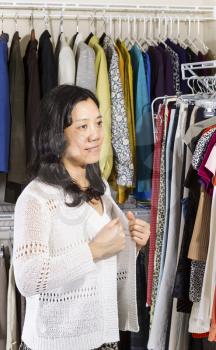 Vertical portrait of mature Asian woman in walk-in closet putting on her white sweater
