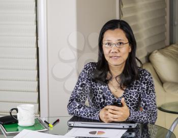 Mature Asian women working from home with cell phone, computer and graphs on table