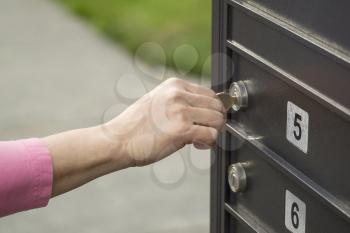 Horizontal photo of female hand putting mailbox key into lock with green grass and sidewalk in background