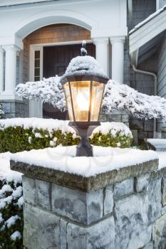 Vertical photo of lamp post, with snow on top, in front of suburban home