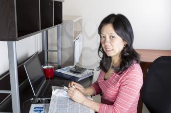 Mature Asian women tearing up tax booklet with computer, calculator, glasses and coffee cup on desk