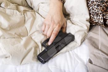 Horizontal photo of female hand holding personal weapon, pistol, while in bed