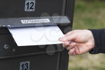 Horizontal photo of male hand putting letters into outgoing postal mailbox with green grass in background