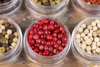 Horizontal top focus shot of  red peppercorns in small container next to other peppercorns on stone surface
