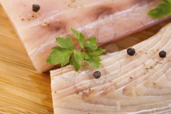 Closeup horizontal photo of white fish fillets, parsley and pepper salts on Natural Bamboo Wood background