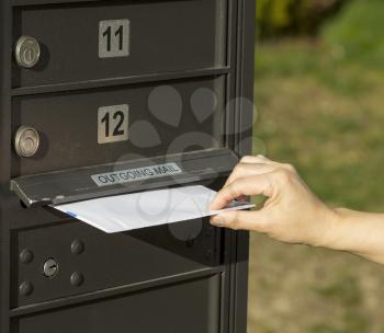 Photo of female hand putting letter into outgoing postal mailbox with green grass in background