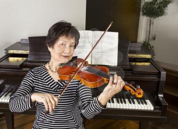 Senior adult woman playing the violin at home with piano in background
