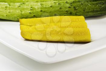 Freshly sliced pickles with cucumber in background on fine white plate