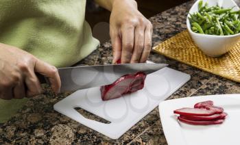 Knife slicing pork meat on white cutting board with green beans in background