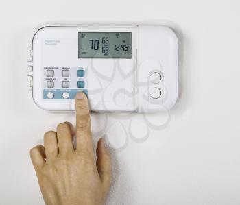Hand adjusting inside home temperature to seventy degrees fahrenheit with White wall as background