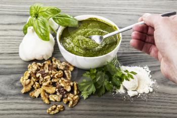 Hand stirring homemade pesto with basil, garlic, walnuts and parsley on aging wood background