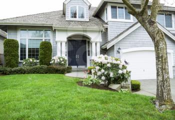 Horizontal photo of modern home in North American Suburbs with plush green grass, rhododendron and tulips flower in mid spring season