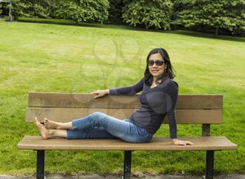 Mature Asian lady resting on cedar bench with lush green grass and trees in background