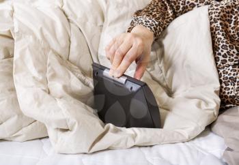 Horizontal photo of female hand pushing down switch on alarm clock to turn it off