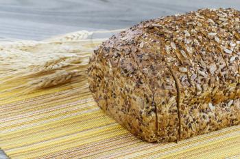 Whole wheat loaf bread sliced with wheat stalks and yellow place mat on wooden table