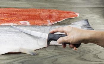 Hand cutting wild salmon into fillets with faded wood in background