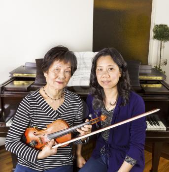Female Violin and piano teachers sitting next to each other with piano in background
