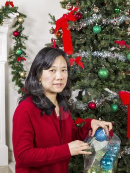Mature Asian woman putting away holiday ornaments in storage container to end the season