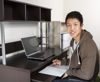 Young Adult Man with pen and paper in hand with computer on desk and wall in background