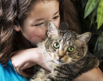 Young Asian girl cuddling tabby cat with green plant in background