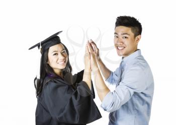 Photo of young adult woman, dressed in graduation gown and cap, receiving congratulations, while both looking forward,  from her boyfriend on a white background