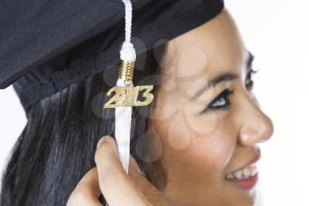 Horizontal photo of male hand holding graduation tassel year date hanging from cap with face of smiling young adult woman in background