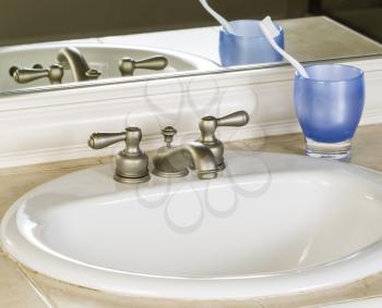 Photo of bathroom sink and faucet with blue cup, tooth brush and mirror in background  