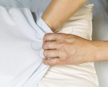 Female hands pulling pillow case over pillow with bed sheets in background