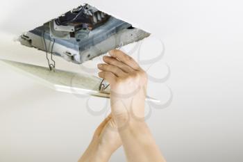 Close up horizontal photo of female hands installing clean bathroom fan vent cover from ceiling 