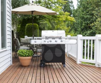 Photo of large barbecue cooker on cedar deck with patio furniture and trees in background  