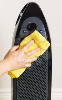 Vertical photo of female hand cleaning home air purifier with yellow microfiber rag with wall in background 