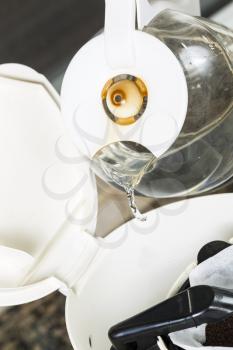 Vertical photo of water being poured, from coffee pot, into coffee maker with fresh coffee grounds in white bleached coffee filter with stone kitchen counter top in background