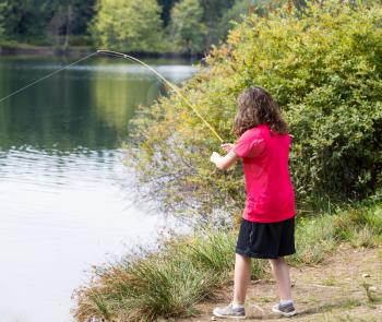 Photo of young girl playing a fish with lake and trees in background 