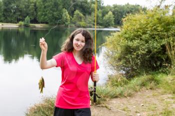 Horizontal photo of a young girl showing her large sunfish that she caught with lake and trees in background 