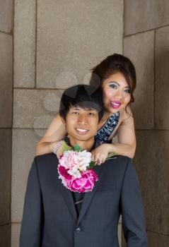 Vertical photo of young adult couple, lady behind man with flowers looking forward, with stone wall in background 